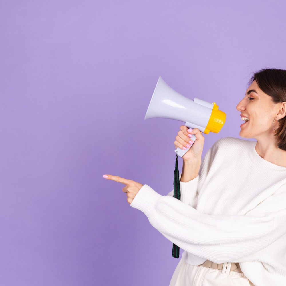 Young brunette in white casual sweater isolated on purple background happy screaming in megaphone copy space point left